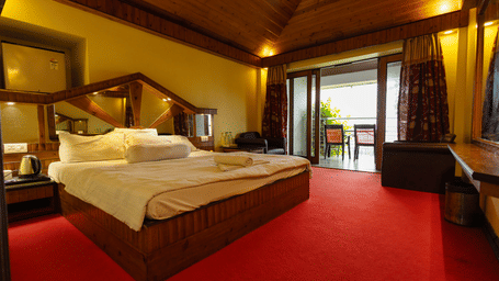 A bedroom with a king size bed, seating area, red carpet, and open balcony door at Hotel Seagull Digha.